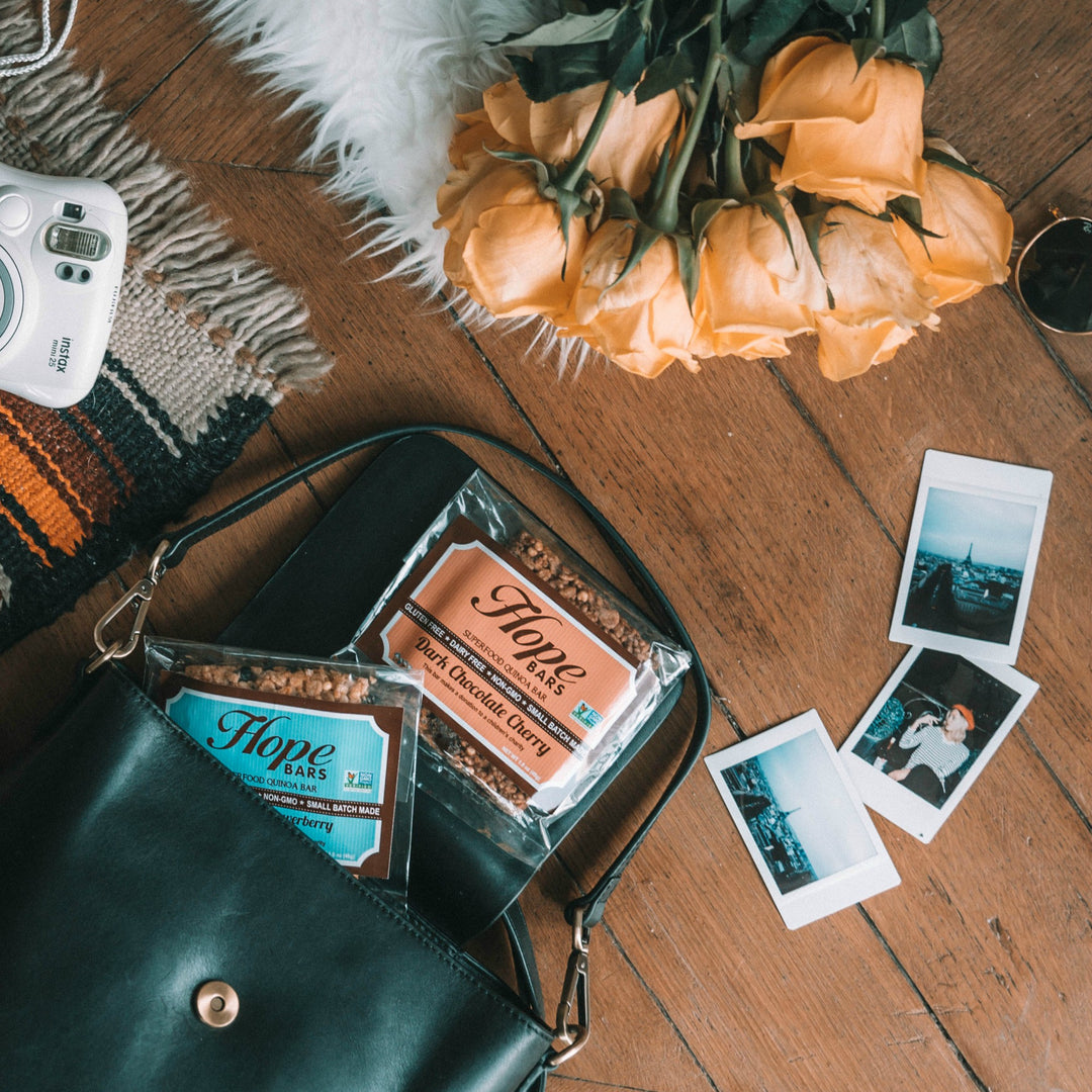 Dark Chocolate Cherry quinoa Hope bars spilling out of a purse next to flowers and pictures