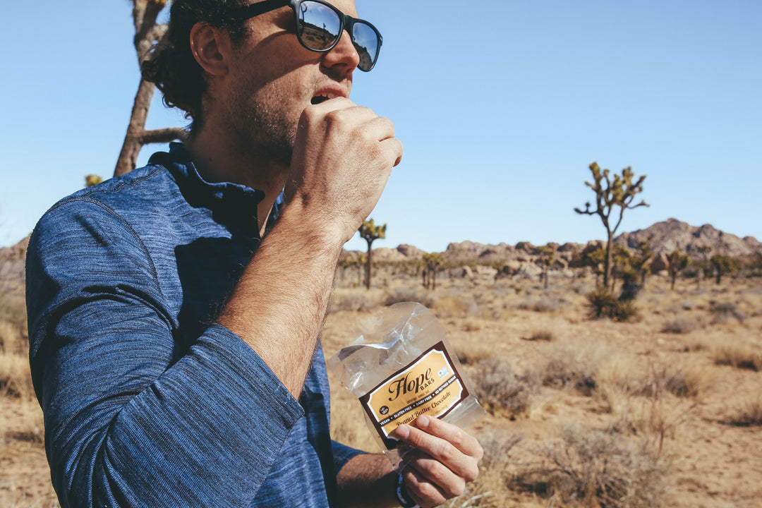 a man eating a Peanut Butter Chocolate Quinoa bar in the desert